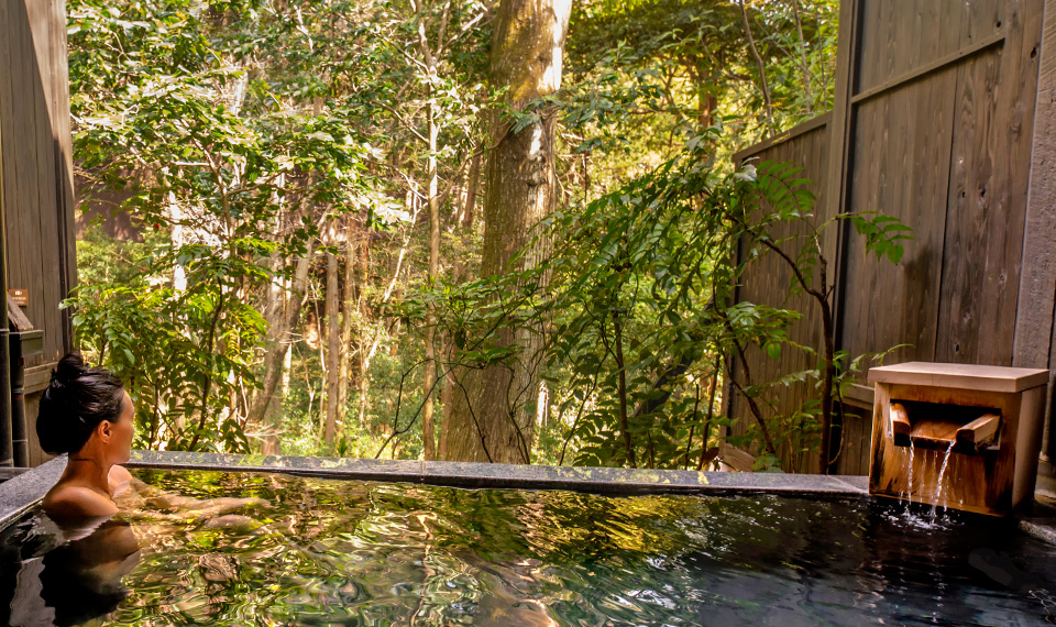 A woman laying in an onsen overlooking the forest