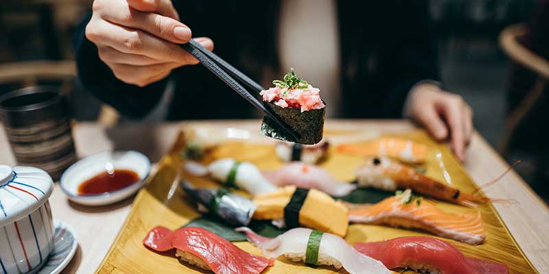 A platter of sushi with someone holding a piece with chopsticks