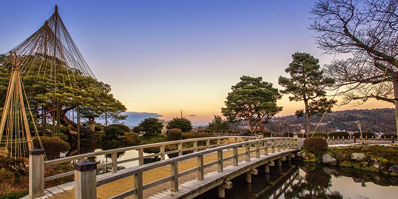A long wooden bridge over water with bamboo structures in the background