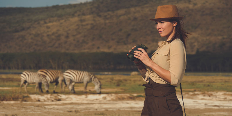A woman holding binoculars with zebras in the background