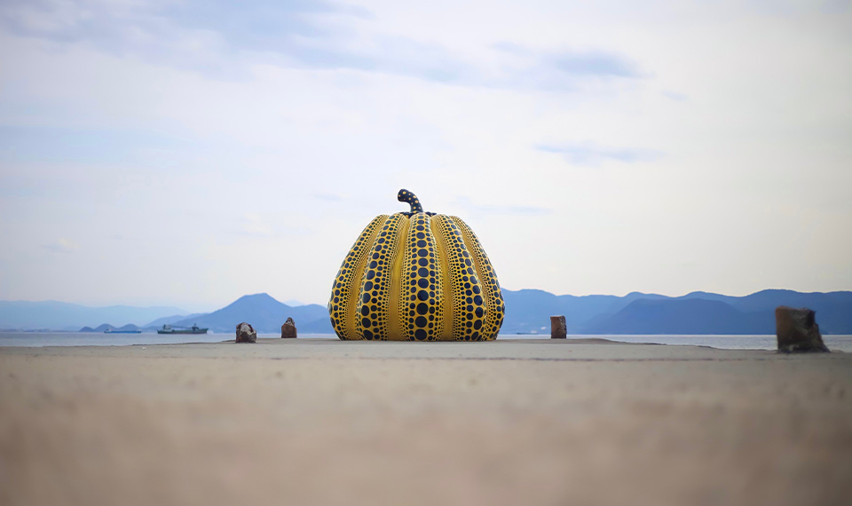 A large ceramic pumpkin sits on a shore