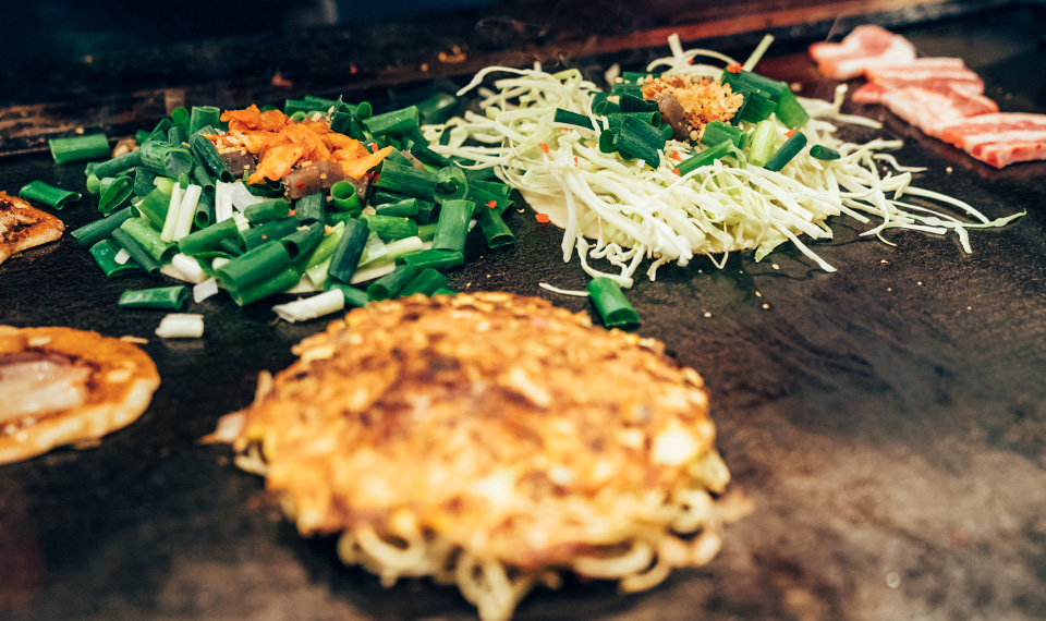 A okonomiyaki on a grill next to some grilled vegetables