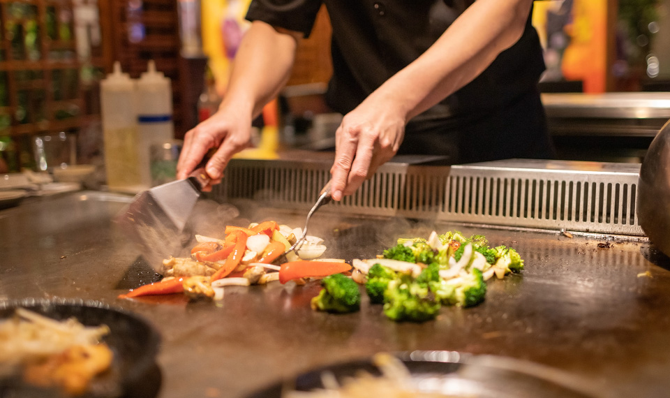 A chef cooking veggies over an open grill