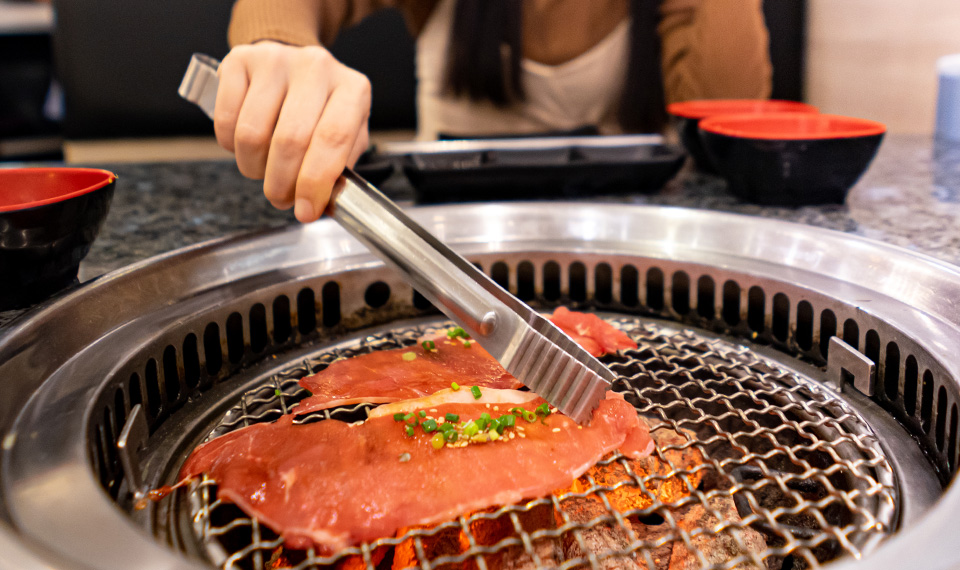 Girl holding tongs placing wagyu steak on a grill