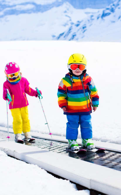 Two kids in ski gear posing near a mountain