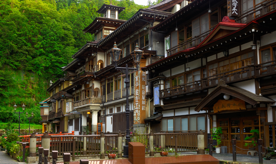 A view of the outside of the Ginzan Onsen with a wooded backdrop