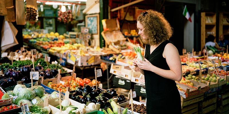 A woman holding vegetables as she peruses a stall