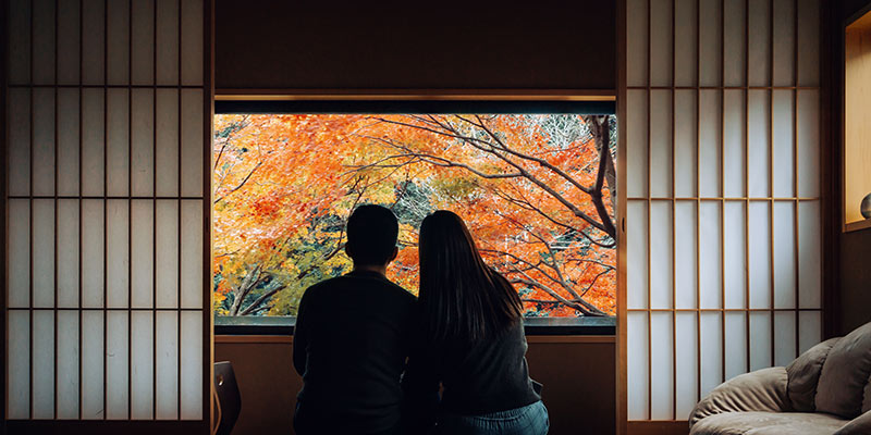 A man and woman look out on colourful trees from their ryokan