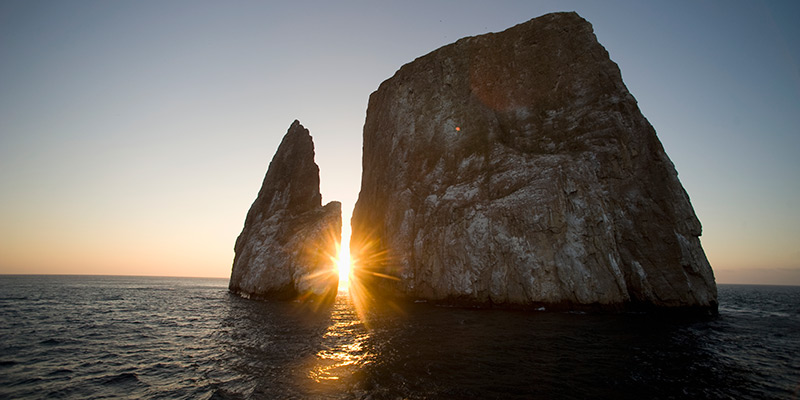 The sun shining between two rocks at sea