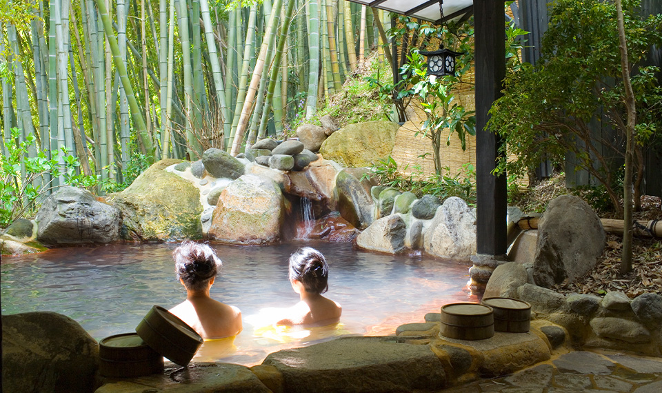 Man and woman in an outdoor onsen with bamboo in the background