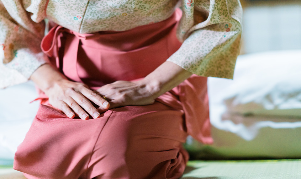 A woman kneeling on the floor with a bed behind her