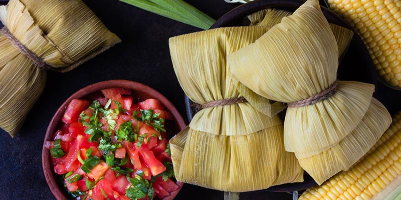 Humitas next to a bowl of fresh tomatoes