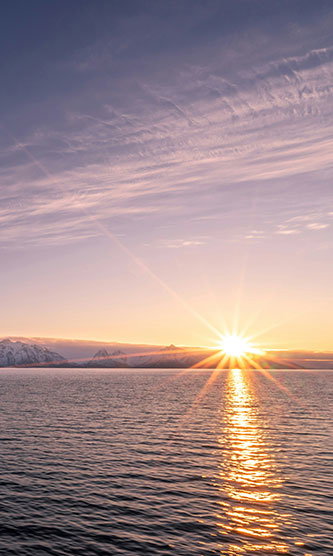 Sun setting over water with snowy mountains in the distance